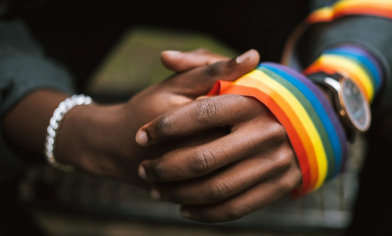 Black hands coming together with rainbow ribbon